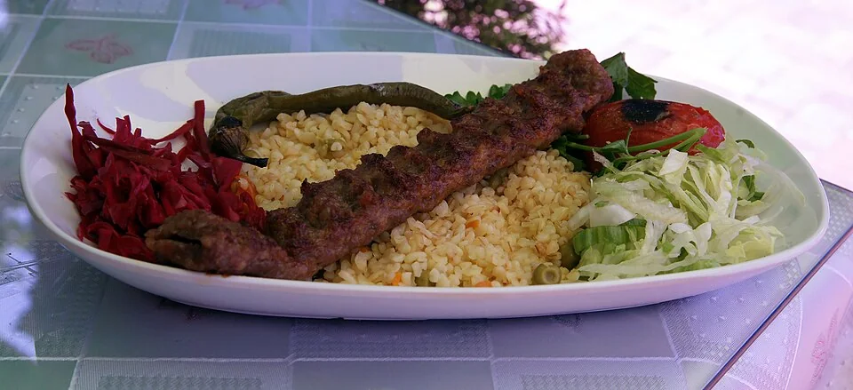 Bulgur pilavı ve sebzelerle servis edilen Adana kebabı tabağı.