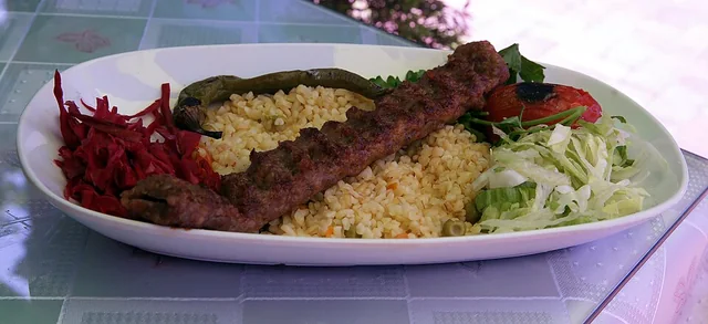 Bulgur pilavı ve sebzelerle servis edilen Adana kebabı tabağı.